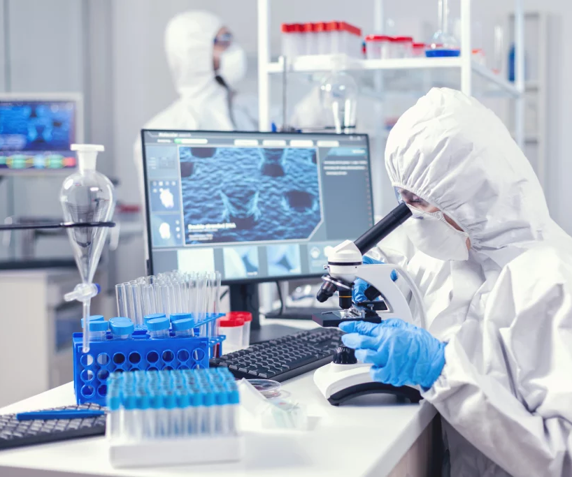 Technicien en combinaison devant un microscope et des ecrans
